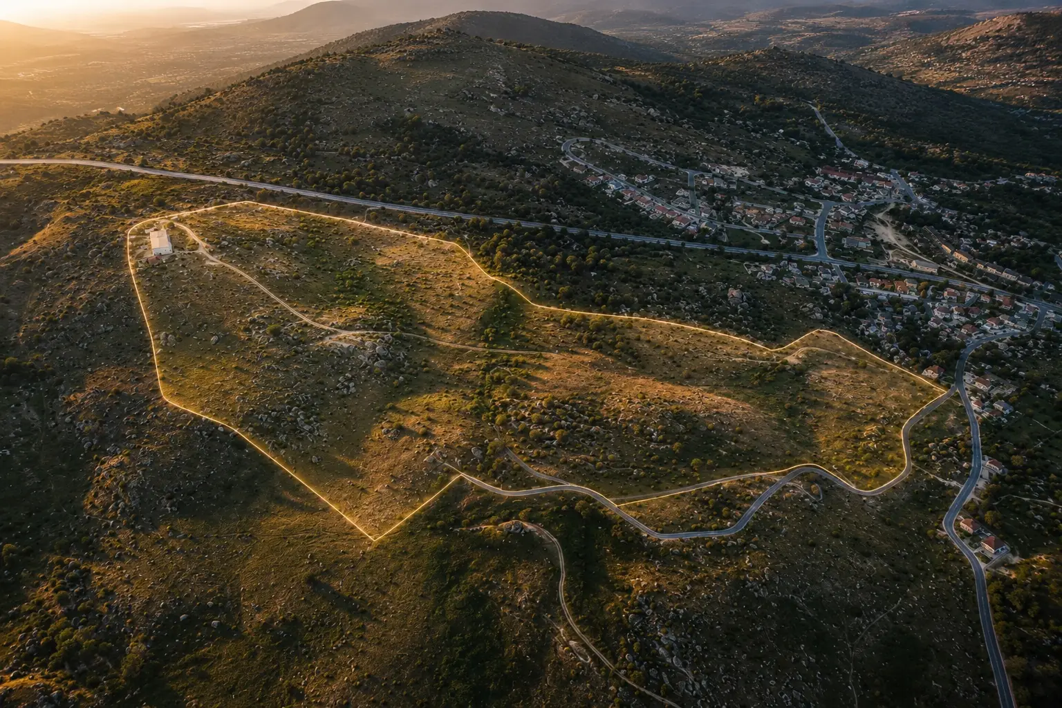 Aerial view at dusk with the estate boundary traced in light, the village of El Boalo beyond