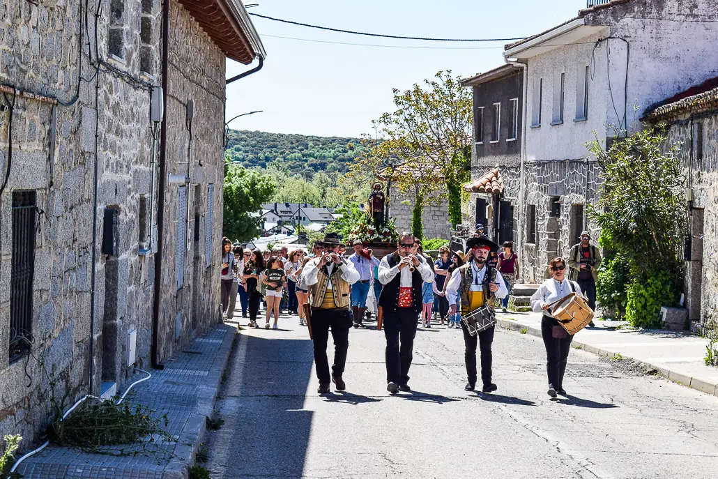 Pipers and drummers in traditional dress leading a fiesta procession up a granite village street